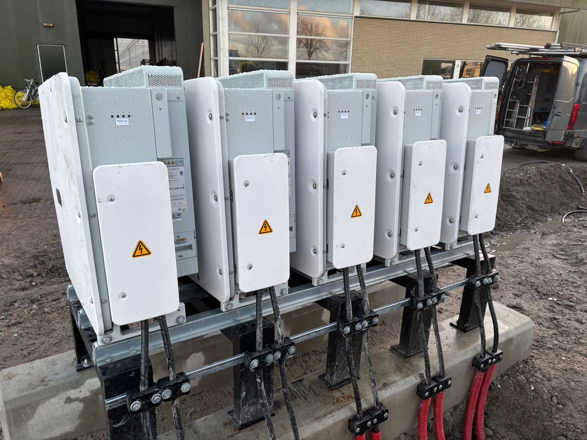 Vijf batterijmodules op een metalen onderconstructie van ROEF, met aangesloten stroomkabels.