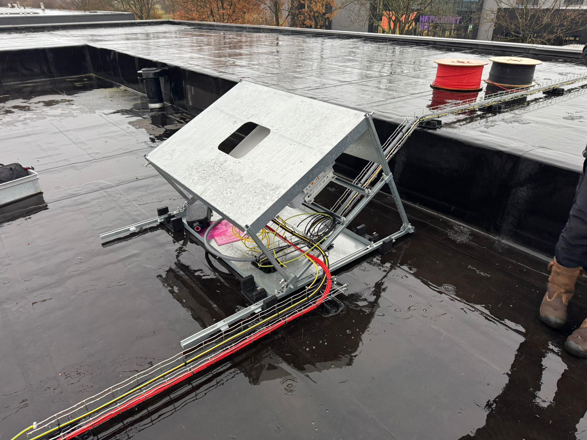 Metalen onderconstructie voor een omvormer op een plat dak, met kabelgoten en bekabeling.
