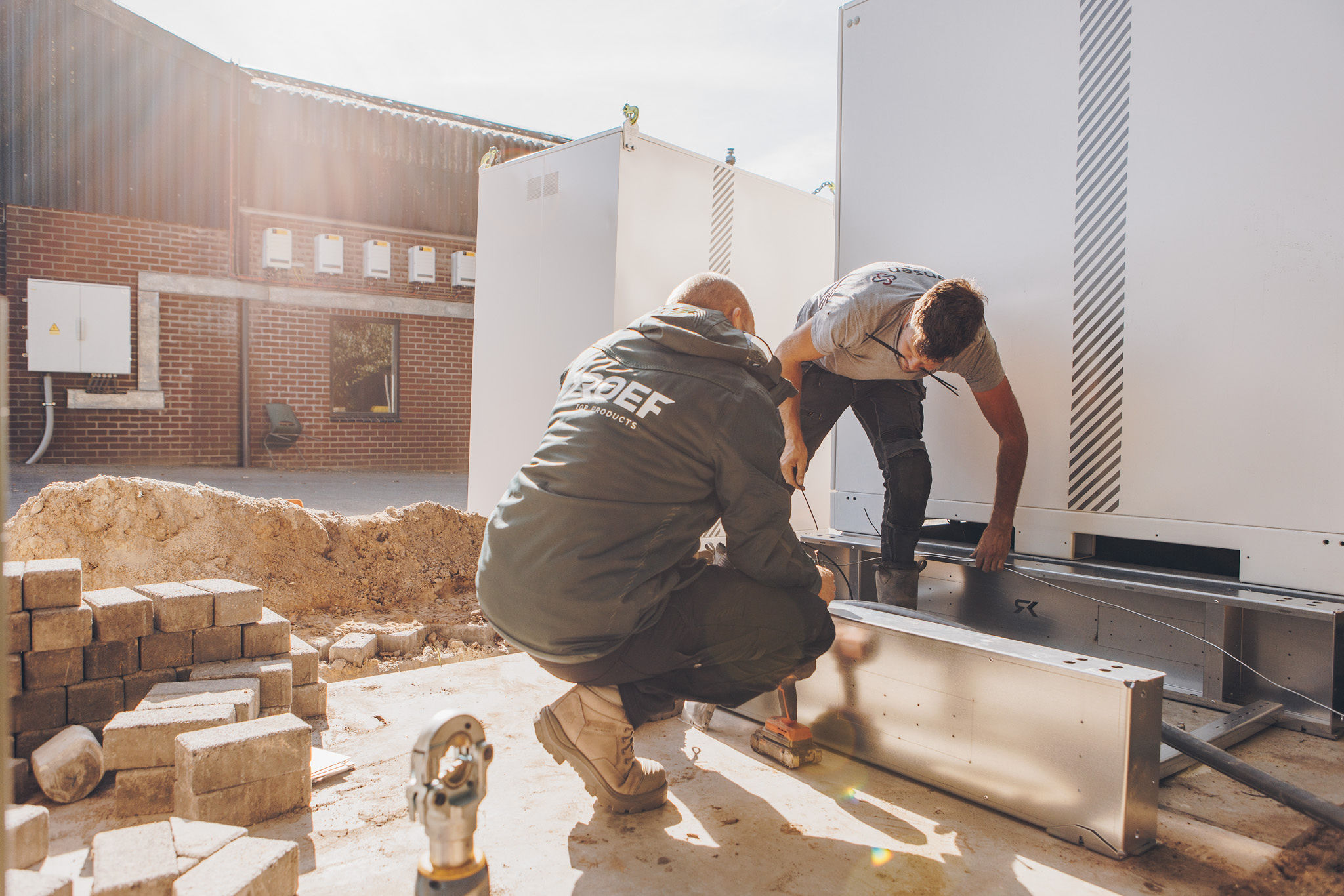 Twee monteurs plaatsen een batterijopslagsysteem op een metalen onderconstructie van ROEF.
